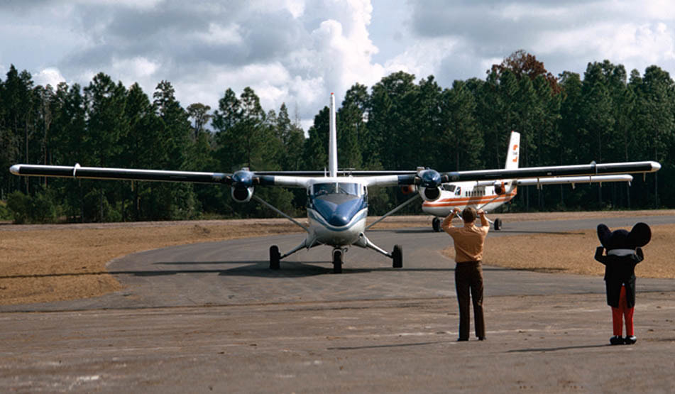 Twin Otters of Executive and Shawnee Airlines are greeted by Mickey Mouse as they arrive at Walt Disney World's Lake Buena Vista STOLport in this 1971 photo.